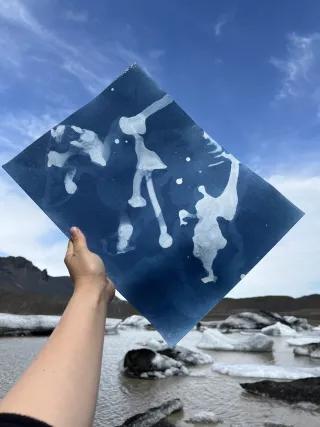 Kunstprojekt Titelbild von Chili Seitz Eine Hand ragt in den Himmel und hält ein Foto von schmelzendem Gletscher hoch