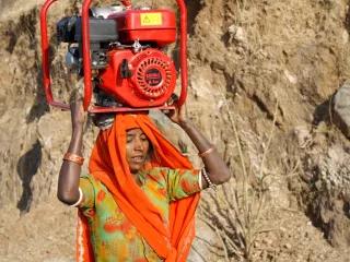 The women of the mountain villages in Rajasthan, India, carry 70 lbs. (or 32kgs) of wood on their heads for cooking every day. This woman is carrying a generator for repair in a nearby village The women of the mountain villages in Rajasthan, India, carry 70 lbs. (or 32kgs) of wood on their heads for cooking every day. This woman is carrying a generator for repair in a nearby village