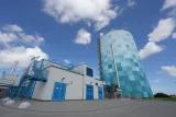 Gigantischer Wärmespeicher in Rostock Dicker Blau-weiß karierter Turm neben einem einem weißem Technik-Gebäude mit blauen Türen und Treppen