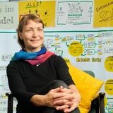 Dr. Gesa Maschkowski sitzt auf einem Stuhl vor einer mit Zetteln beklebten Wand.