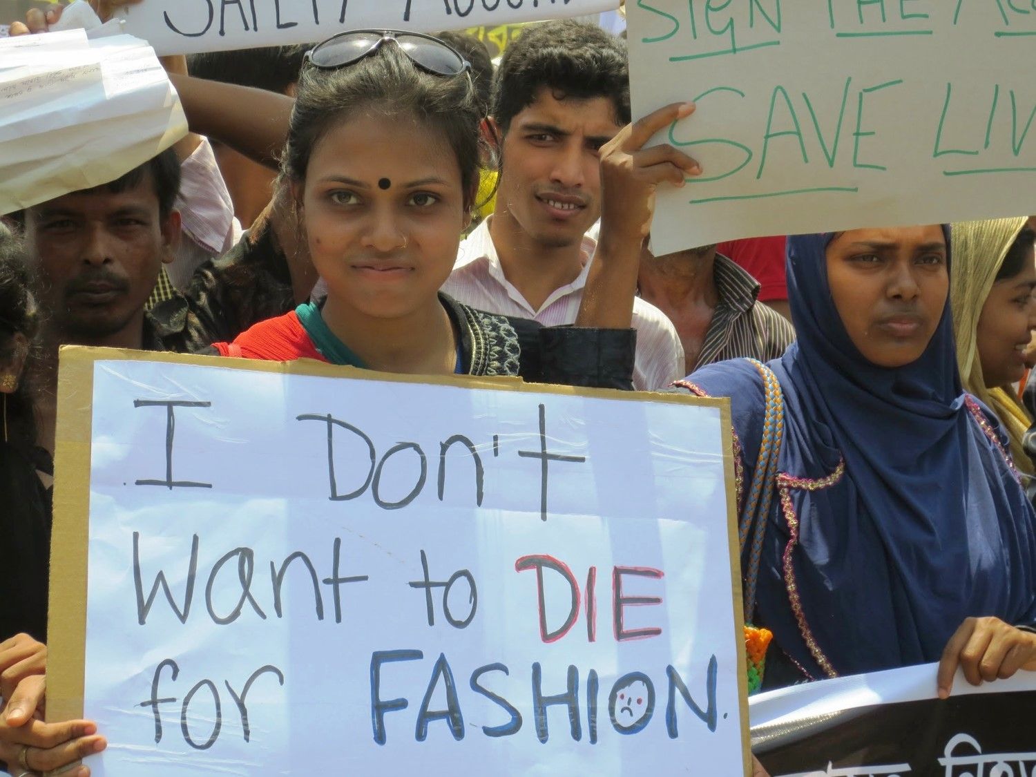 Arbeiter/innenprotest nach dem Einsturz des Rana-Plaza-Gebäudes in Bangladesch Eine Frau steht in einer Menge Protestant/innen und hält ein Plakat mit der Aufschrift "I don't want to die for fashion".
