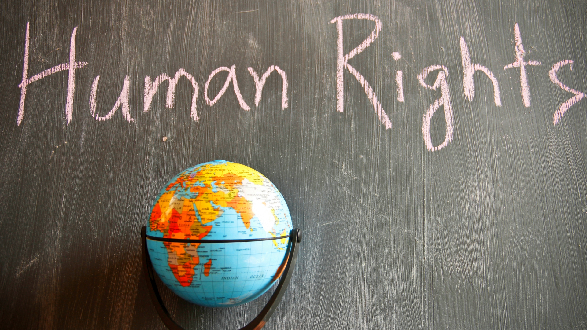 Globale Menschenrechte Ein Globus vor einer braunen Wand auf der Human Rights geschrieben steht.